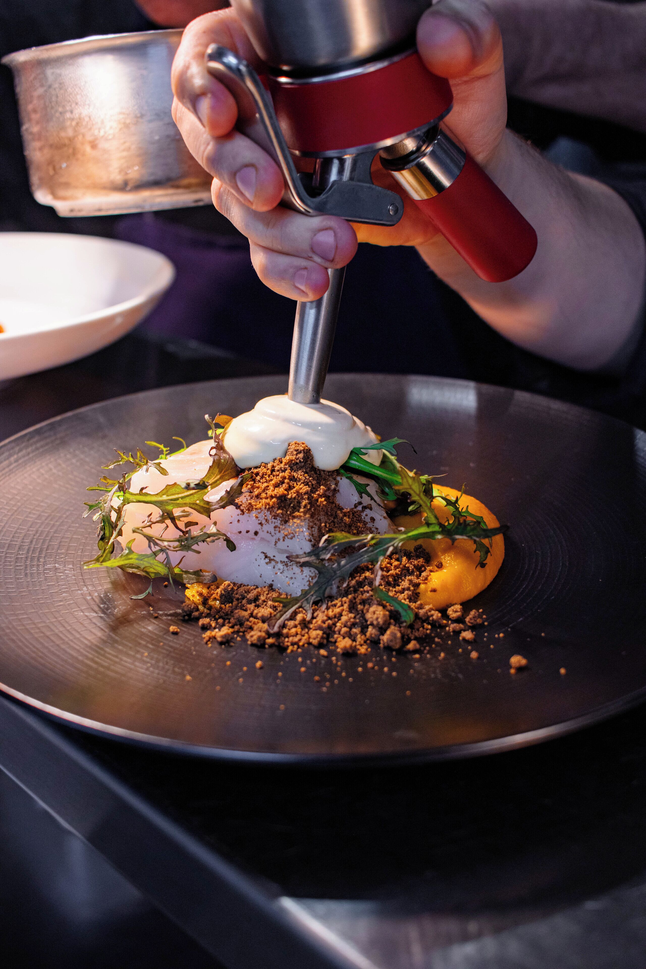 A person pouring a sauce from a red and silver bottle onto a plate with food.