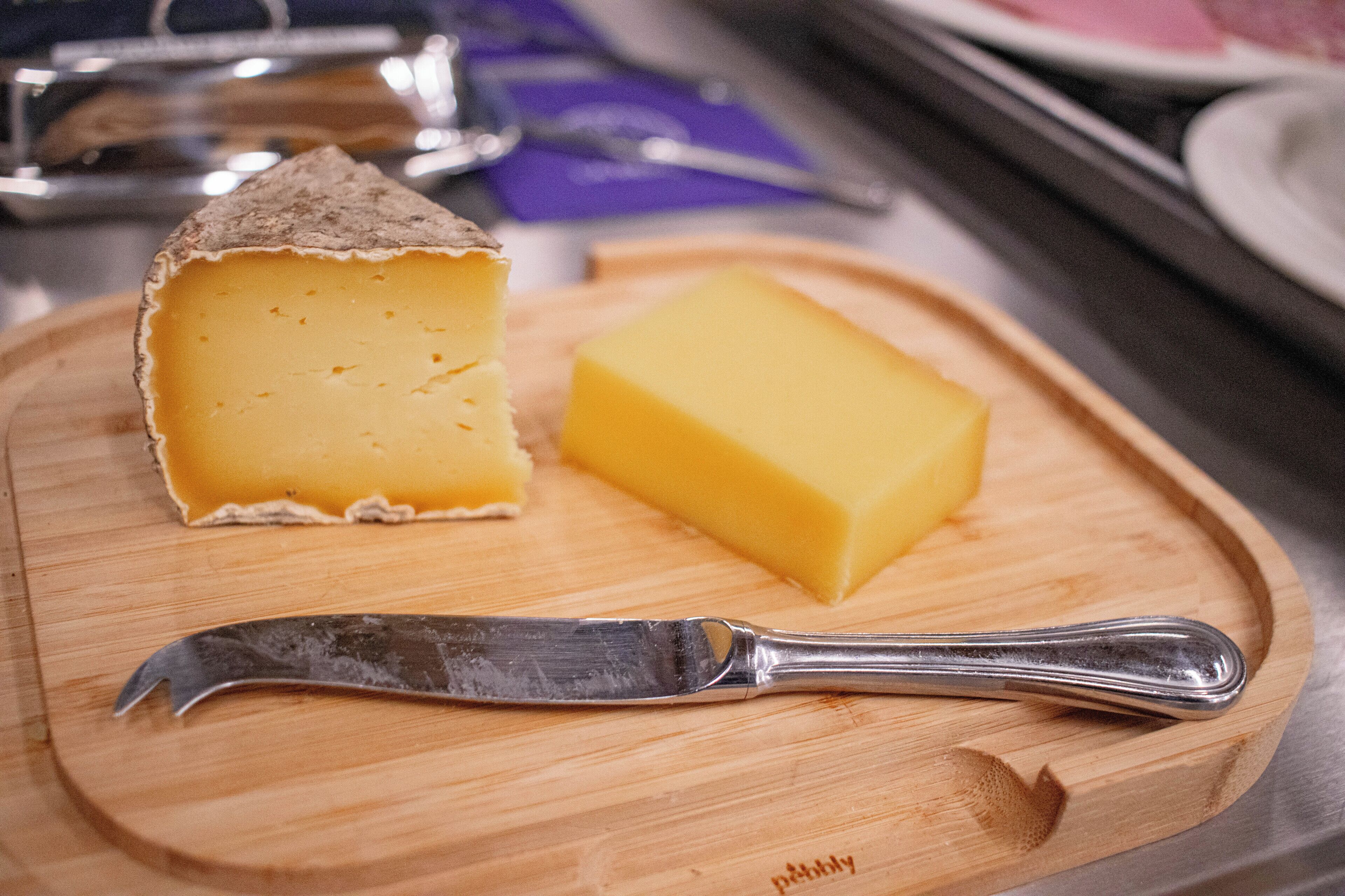 A cheese on a wooden cutting board with a knife beside it.