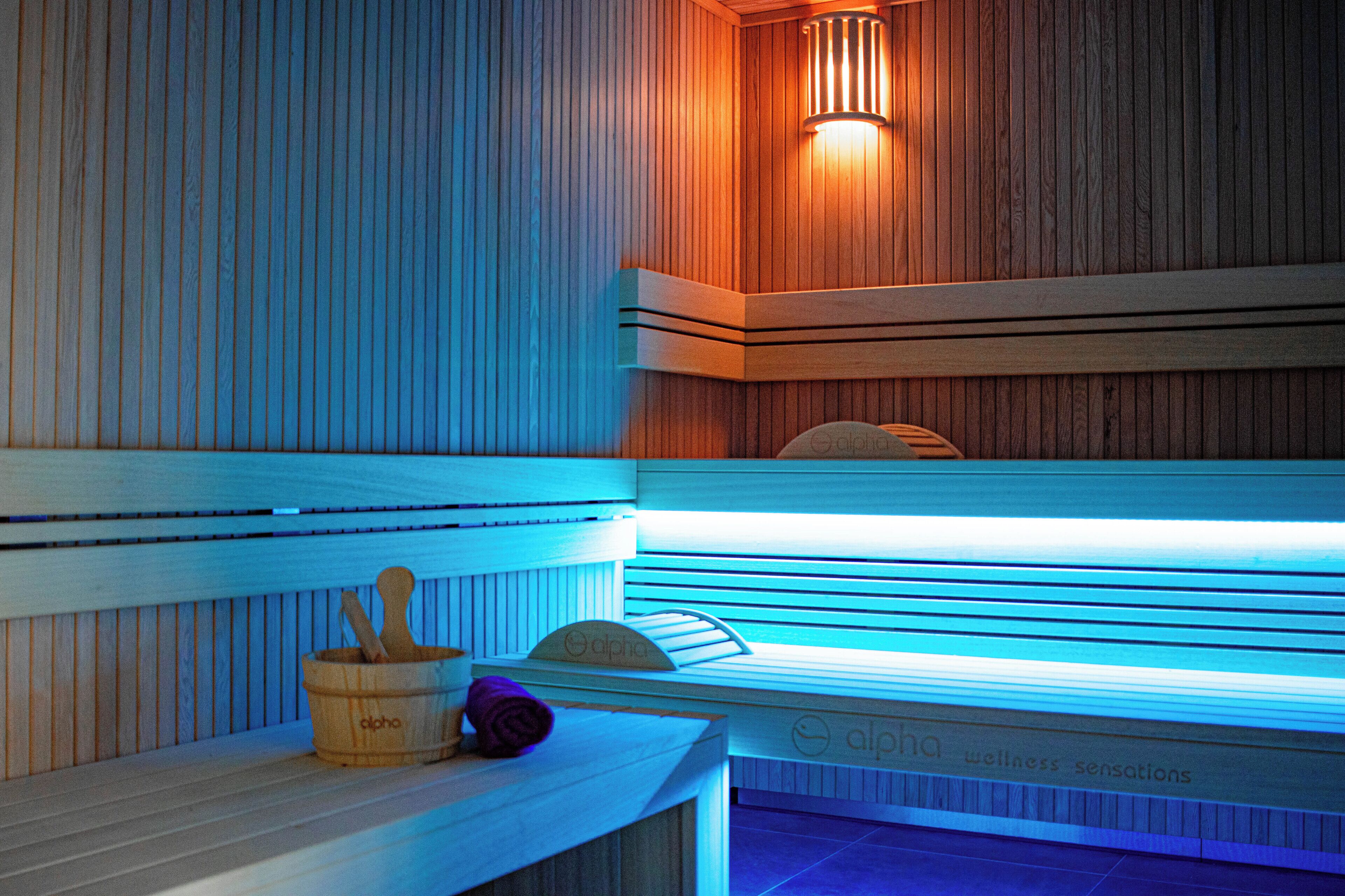 A wooden sauna with benches, a wall-mounted heater, and a wooden bucket with a brush.