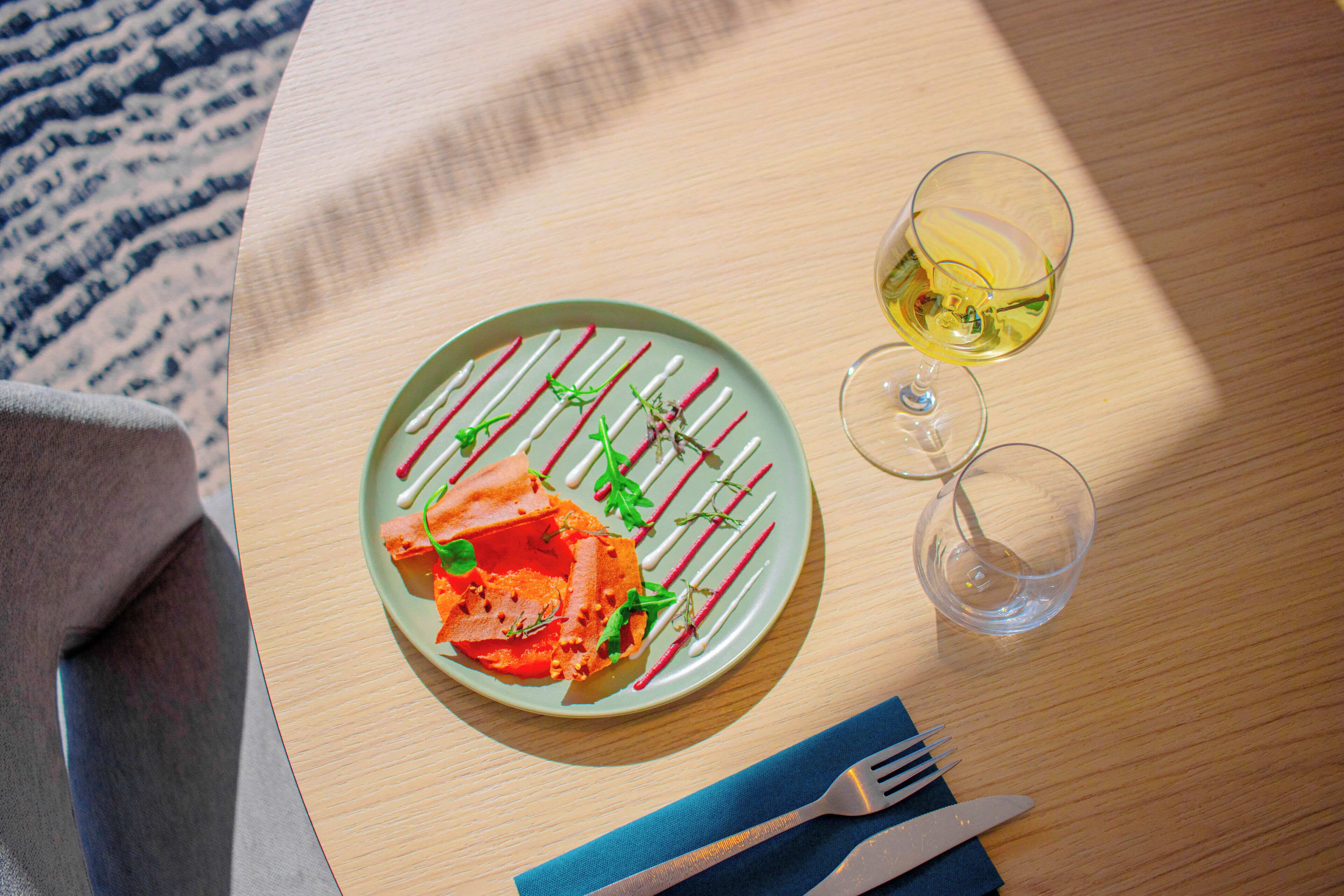 A plate of food with a fork and knife, a glass of wine, and a blue napkin on a wooden table.