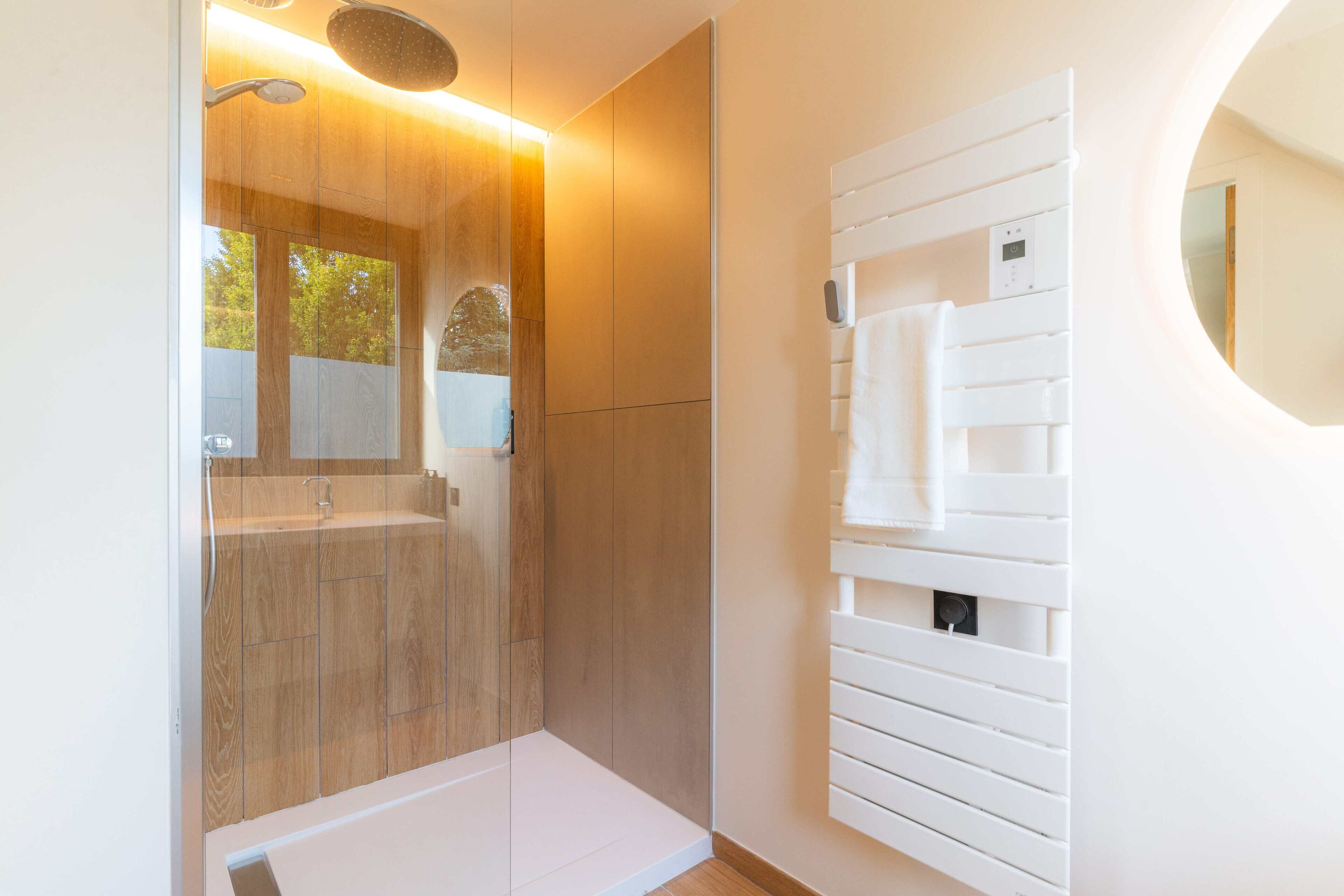 Un baño moderno con ducha de vidrio, tocador blanco con espejo y un perchero para toallas.