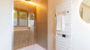 Un baño moderno con ducha de vidrio, tocador blanco con espejo y un perchero para toallas.