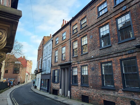 A street with historic brick buildings, including a row of shops and a building with a large window.