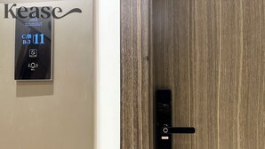 Ein Hotelzimmer mit einer Holztür und einem an der Wand montierten Gegensprechanlage mit den Aufschriften 'Kease' und 'Alma Diah Residence'.