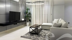 Ein modernes Wohnzimmer mit Flachbildfernseher, einer Couch, einem Couchtisch und einer Topfpflanze.