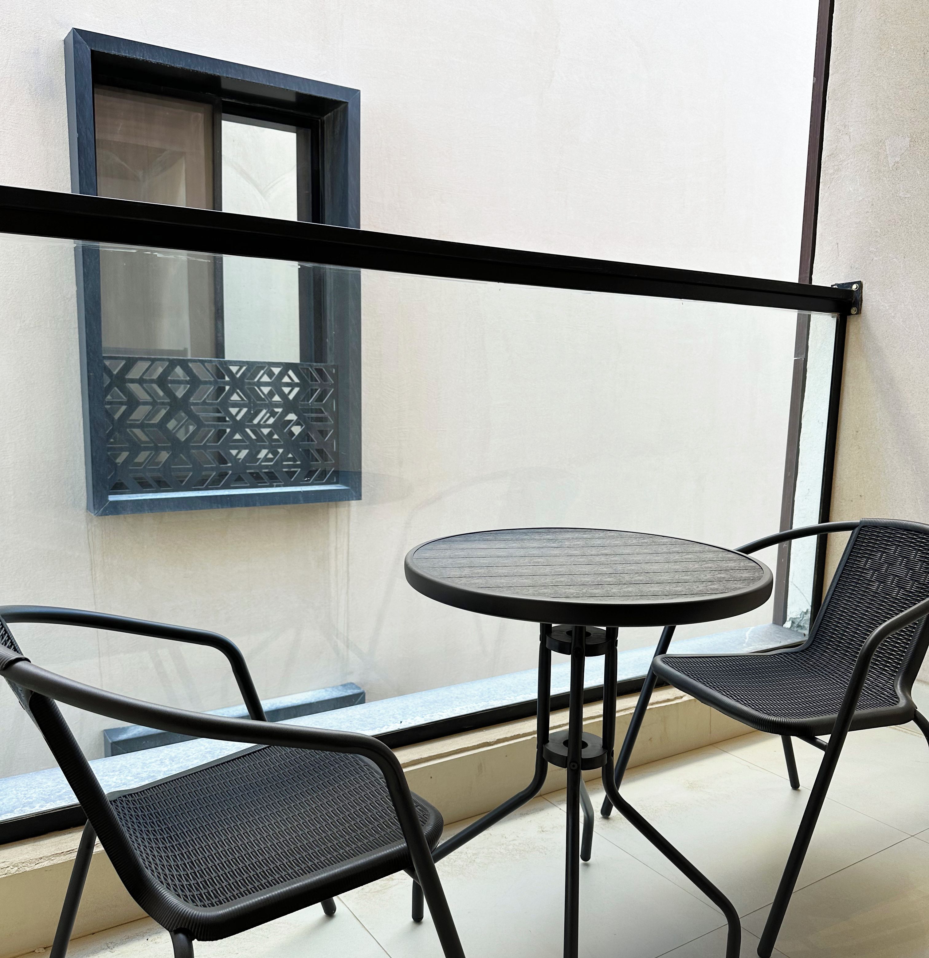 A balcony with a round table and two chairs, a window with a geometric pattern, and a sign reading "Kease".