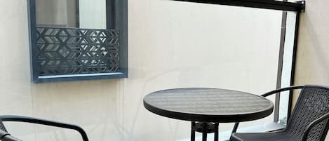 A balcony with a round table and two chairs, a window with a geometric pattern, and a sign reading "Kease".