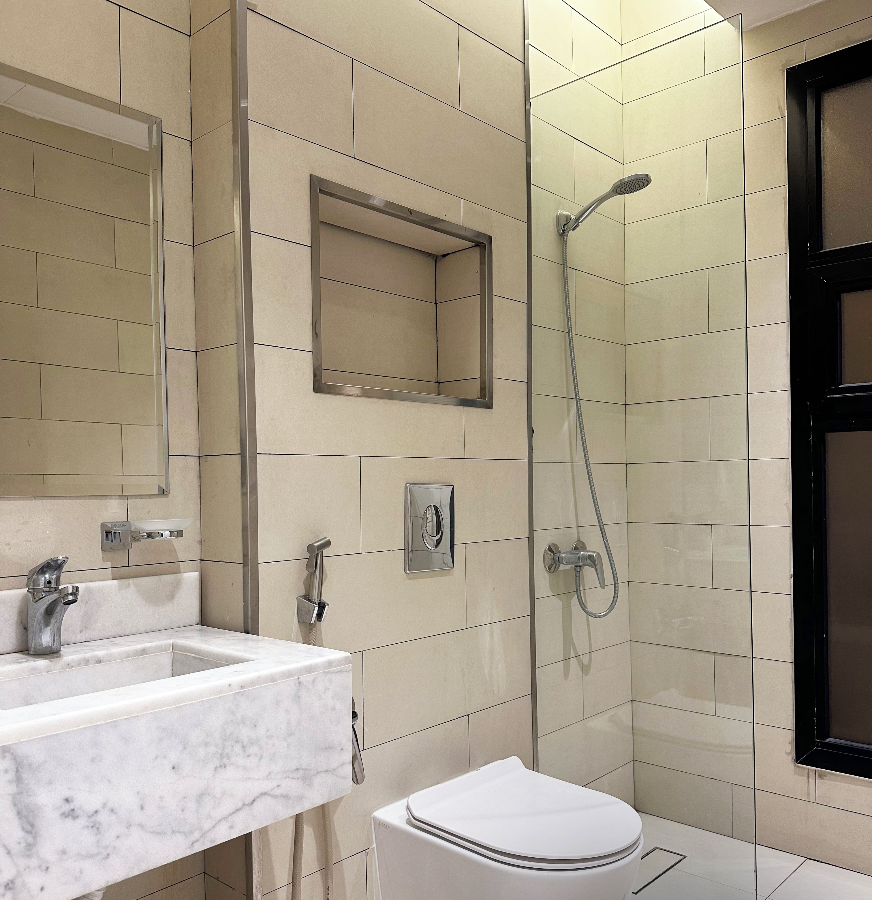 Et moderne badeværelse med vask i marmor, toilet og bruseniche.
