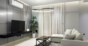 Un salon moderne avec un téléviseur à écran plat, un canapé, une table basse et une plante en pot.