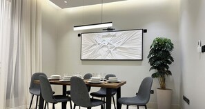Un espace repas moderne avec une table rectangulaire, quatre chaises grises à revêtement rembourré et un grand tableau abstrait accroché au-dessus de la table.