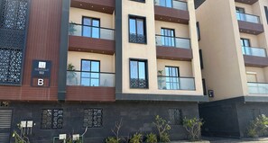 Un immeuble résidentiel à plusieurs étages, doté de balcons, d’une enseigne indiquant « Zone 01 » et offrant une vue partielle sur une entrée fermée par un portail.