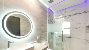 Une salle de bain moderne avec un miroir rond, une douche en verre et un lavabo blanc.