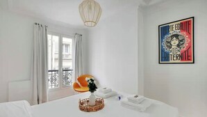 A hotel room with a bed, a vase with flowers, a framed picture on the wall, and a window with curtains. - Le Petit Palais de L'élysée (Paris)