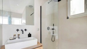 A modern bathroom with a large white sink, a mirror, and a glass-enclosed shower. - Le Petit Palais de L'élysée (Paris)