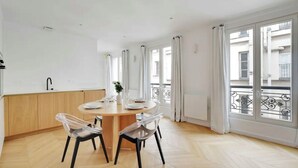 A modern kitchen with a round dining table, clear chairs, and large windows with curtains. - Le Petit Palais de L'élysée (Paris)