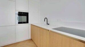 A modern kitchen with white cabinetry, a built-in oven, a black faucet, and a wooden countertop. - Le Petit Palais de L'élysée (Paris)