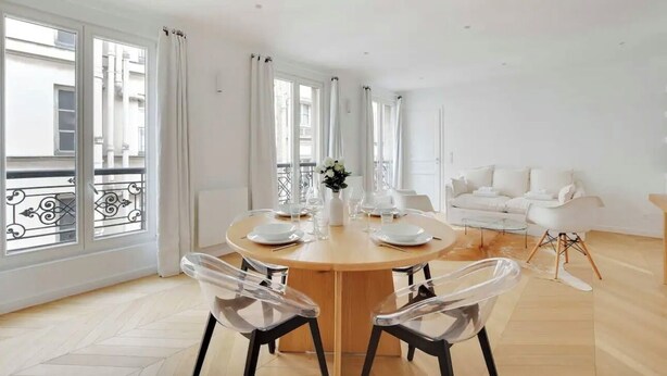 A modern dining area with a round table, clear chairs, and a white sofa in the background. - Le Petit Palais de L'élysée (Paris)