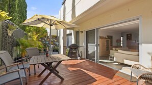 Une terrasse extérieure dotée d'une plateforme en bois, de meubles en osier, d'un barbecue et d'une porte-fenêtre coulissante donnant sur un espace de vie.