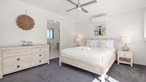 Une chambre à coucher comprenant un lit, des tables de chevet, une commode, un ventilateur de plafond et un élément de décoration murale.