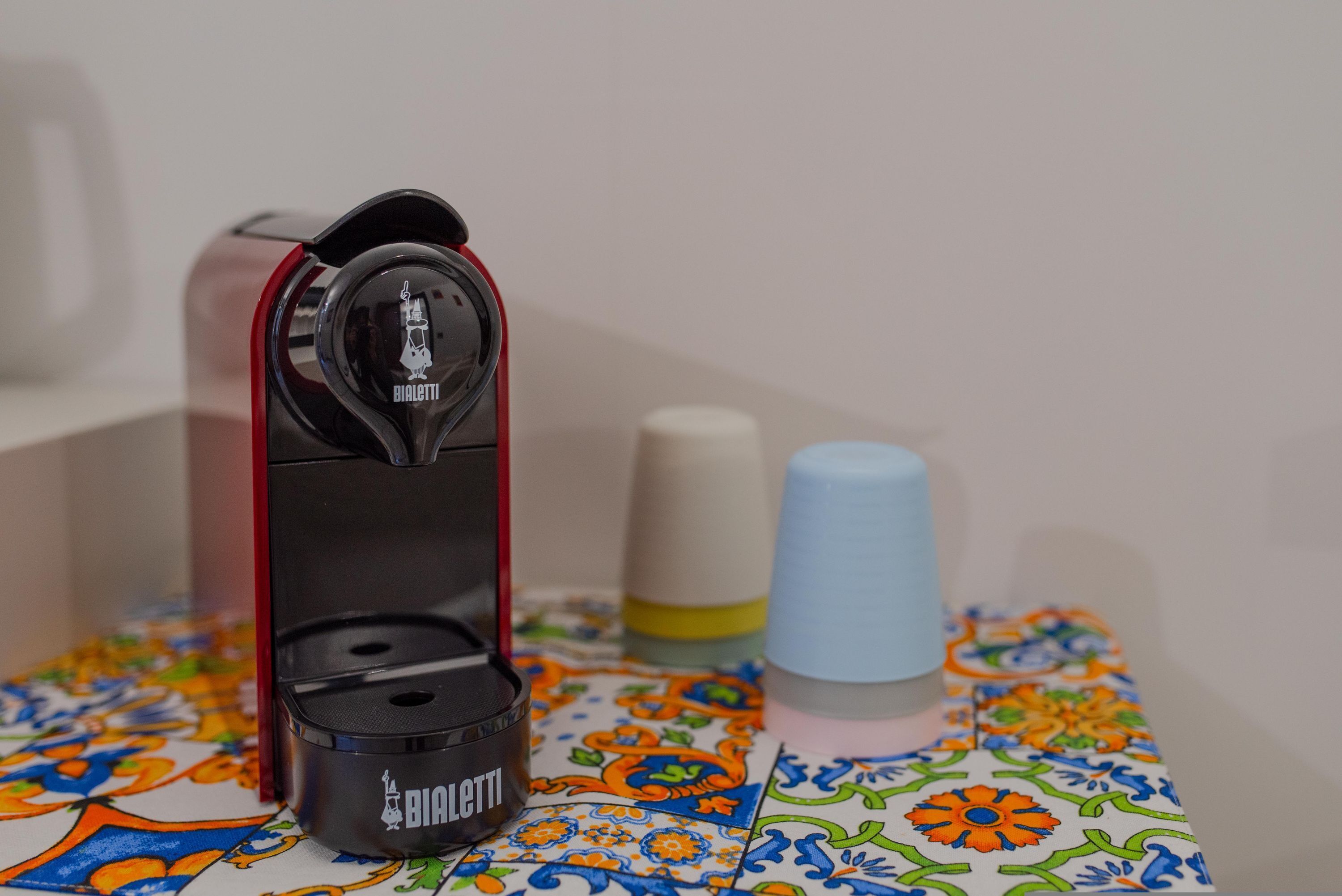 Una máquina de café con base roja y parte superior negra, sobre una mesa de azulejos coloridos.