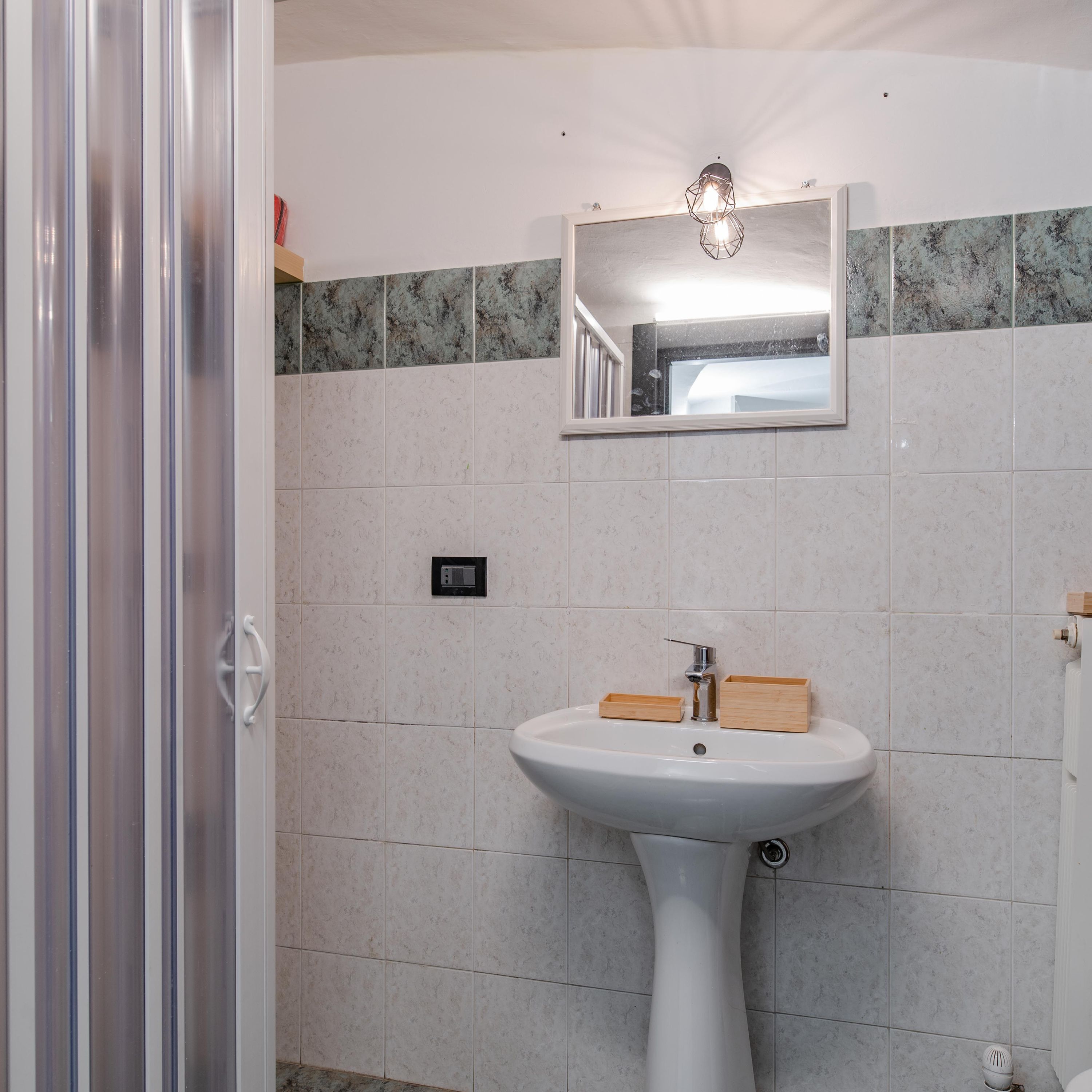 Un baño con un lavamanos pedestal blanco, un espejo encima y una zona de ducha a la izquierda.