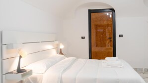 Moderni hotellihuone, jossa on suuri sänky, yöpöytävalaisimet, puinen ovi ja valkoinen seinä.