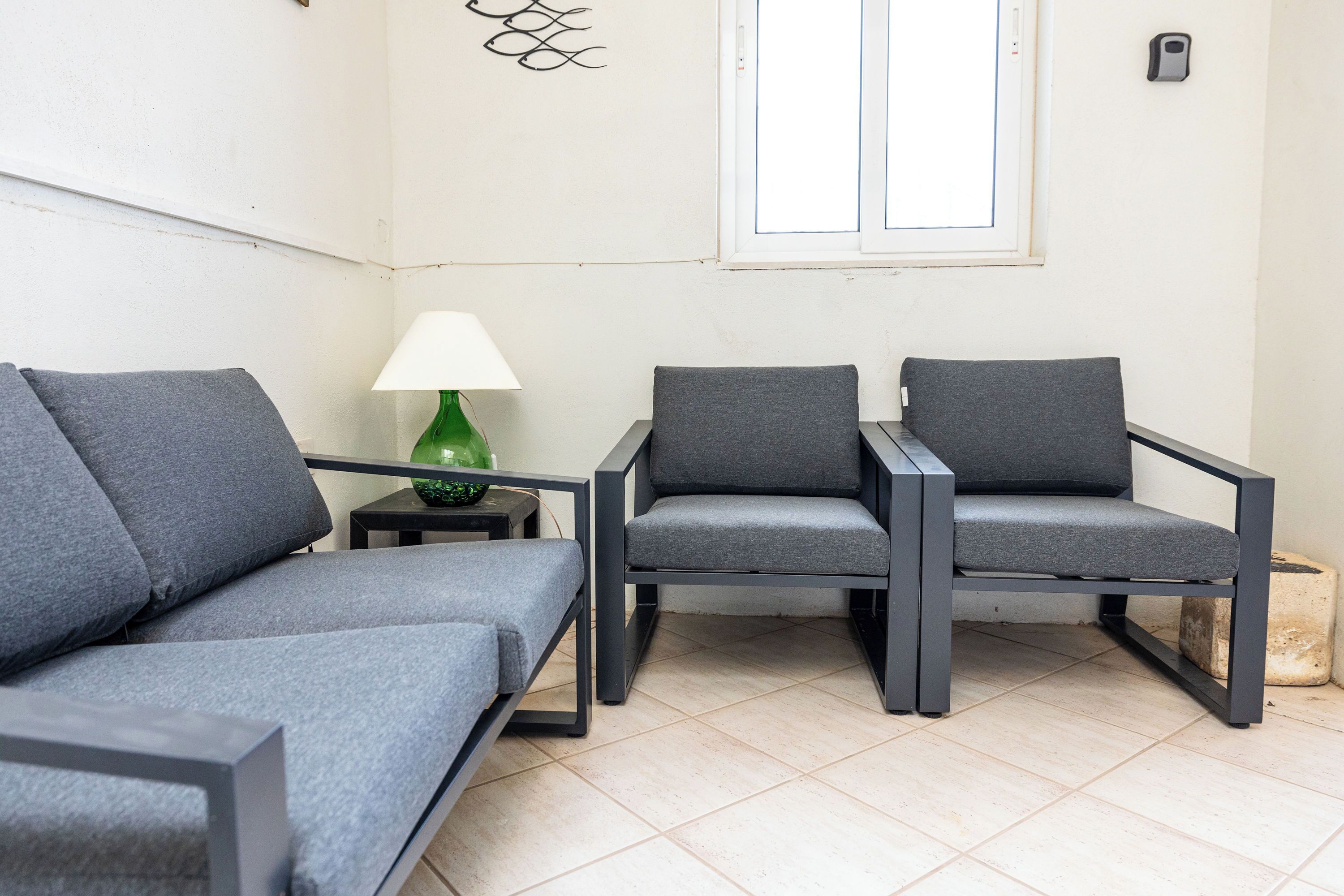 A room with two grey sofas, a green table lamp, and a window with blinds.