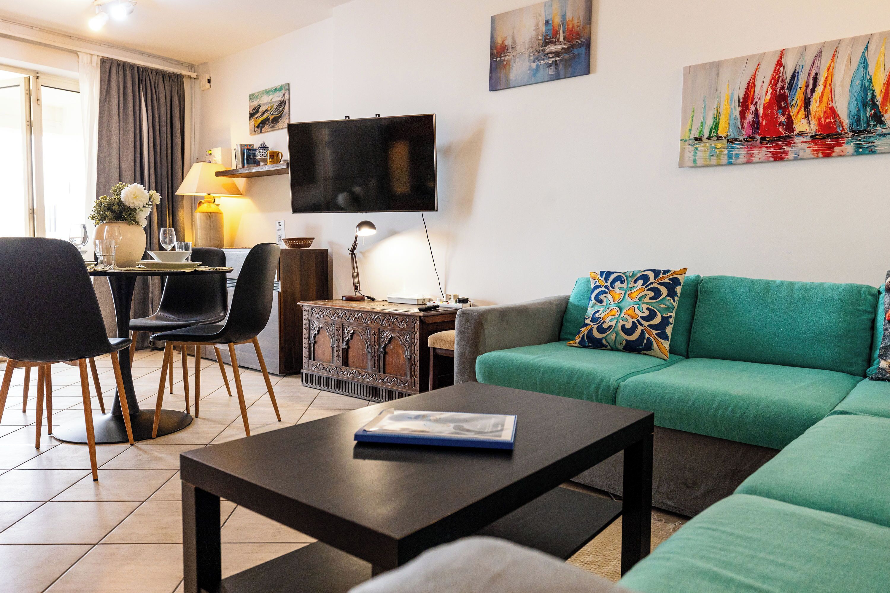Ein Wohnzimmer mit grünem Sofa, einem Couchtisch, einem Fernseher und einem Essbereich mit Stühlen und einem Tisch.
