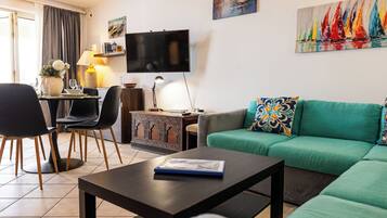 Un salon avec un canapé vert, une table basse, un téléviseur et un coin repas comprenant des chaises et une table.