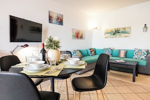 Un salon moderne comprenant un coin repas, un téléviseur à écran plat fixé au mur et un canapé agrémenté de coussins colorés.