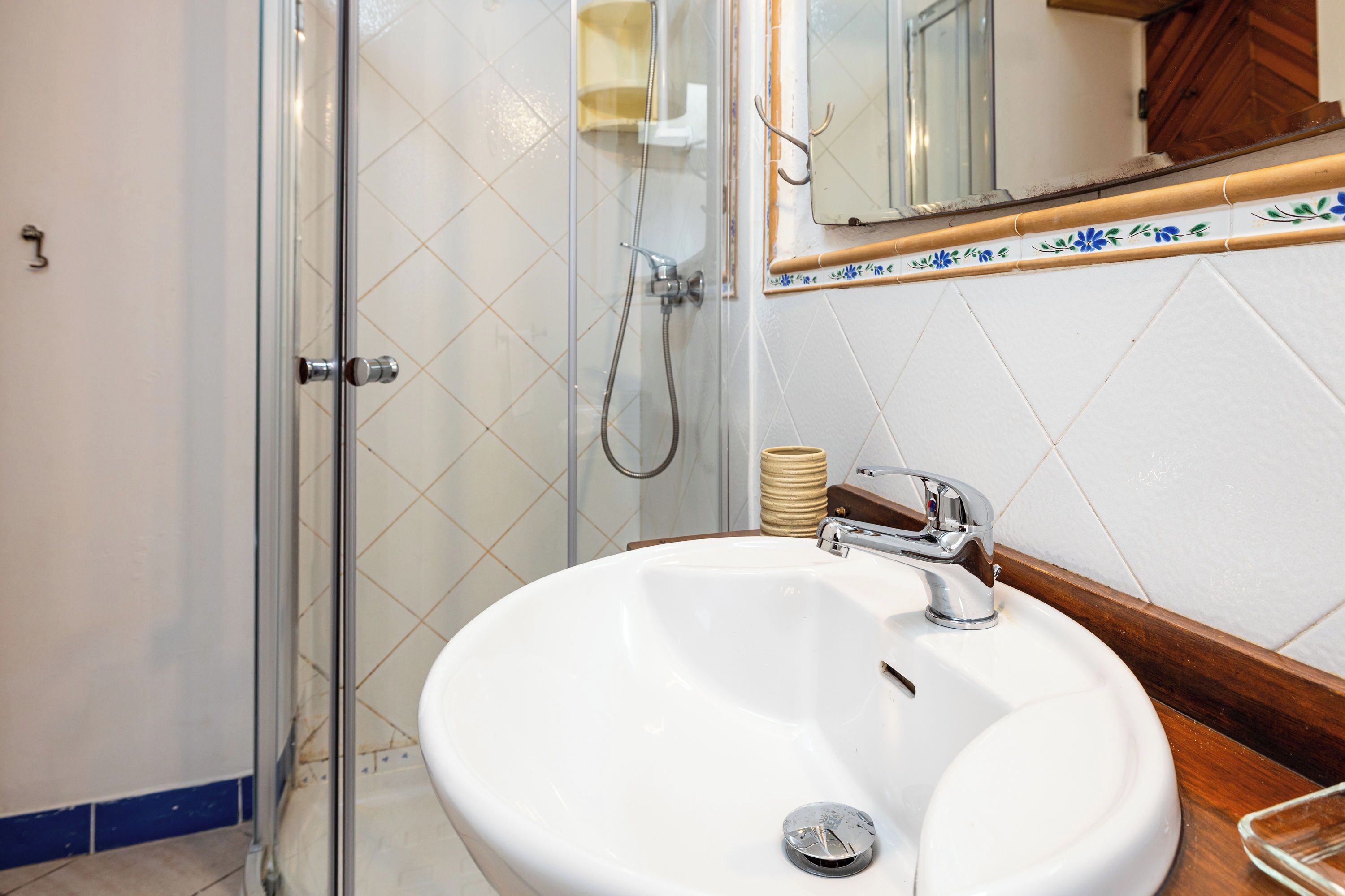 Un baño con mampara de vidrio, un lavabo blanco con grifo cromado y un espejo sobre el lavabo.