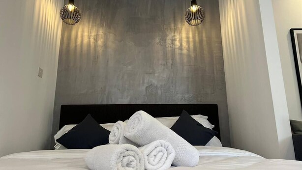 Hotellihuone, jossa on sänky, kaksi riippuvalaisinta ja kuvioitu seinä.