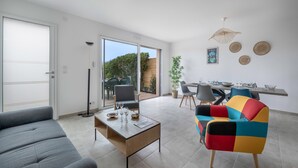 A modern living room with a grey sofa, a colorful armchair, a wooden coffee table, and a dining area with a table and chairs. - Recent house in Pornic, 500m from the beach for 5 (Pornic)