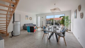 A modern kitchen with a built-in stove, a dining area with a large table and chairs, and a staircase leading to an upper level. - Recent house in Pornic, 500m from the beach for 5 (Pornic)
