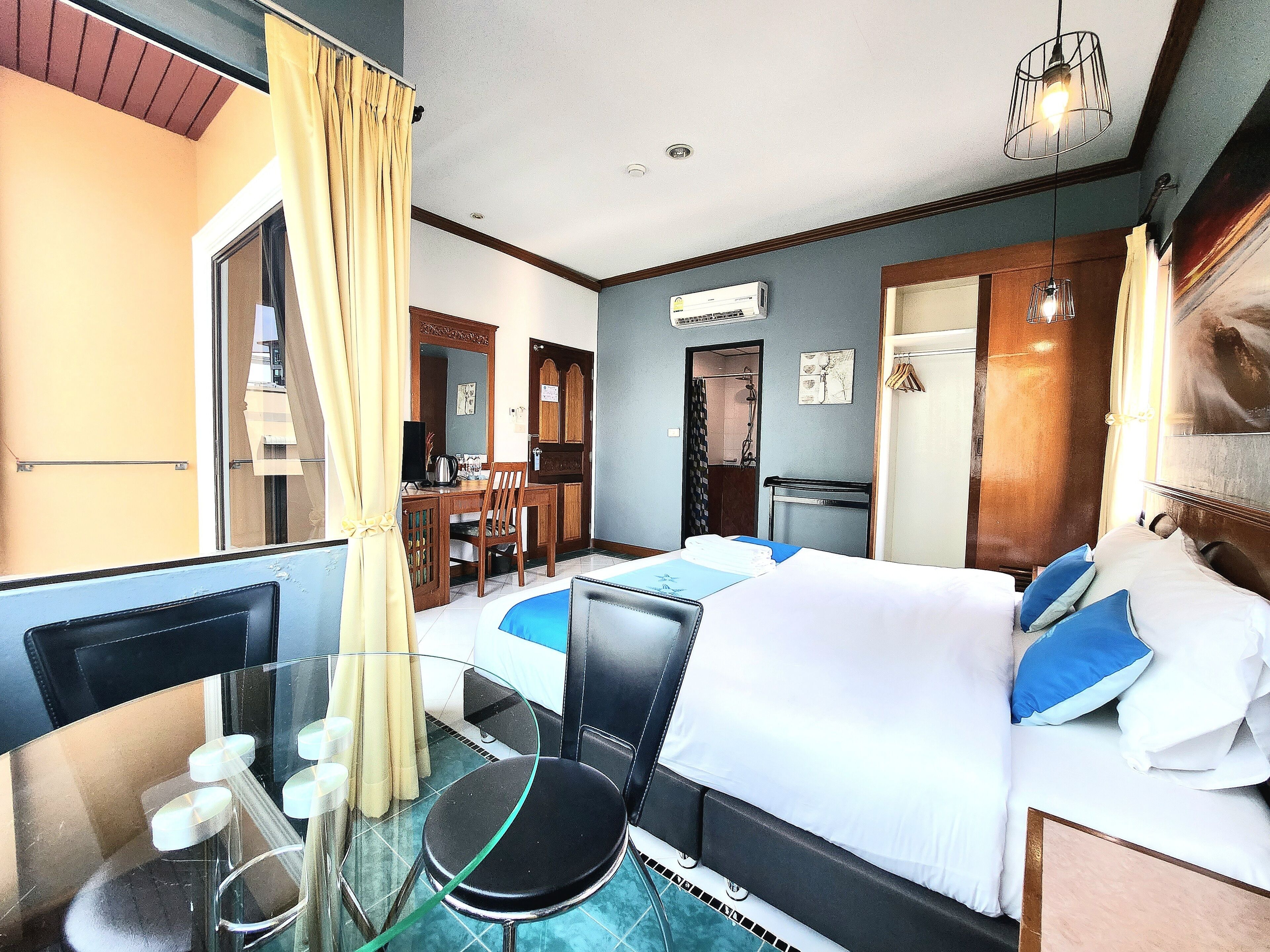 Habitación de hotel con cama, escritorio, silla, mesa de vidrio y baño visible a través de una puerta abierta.