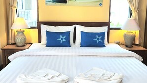 Una habitación de hotel con una cama, dos mesitas de noche, un cuadro de un bote en la playa y cortinas.
