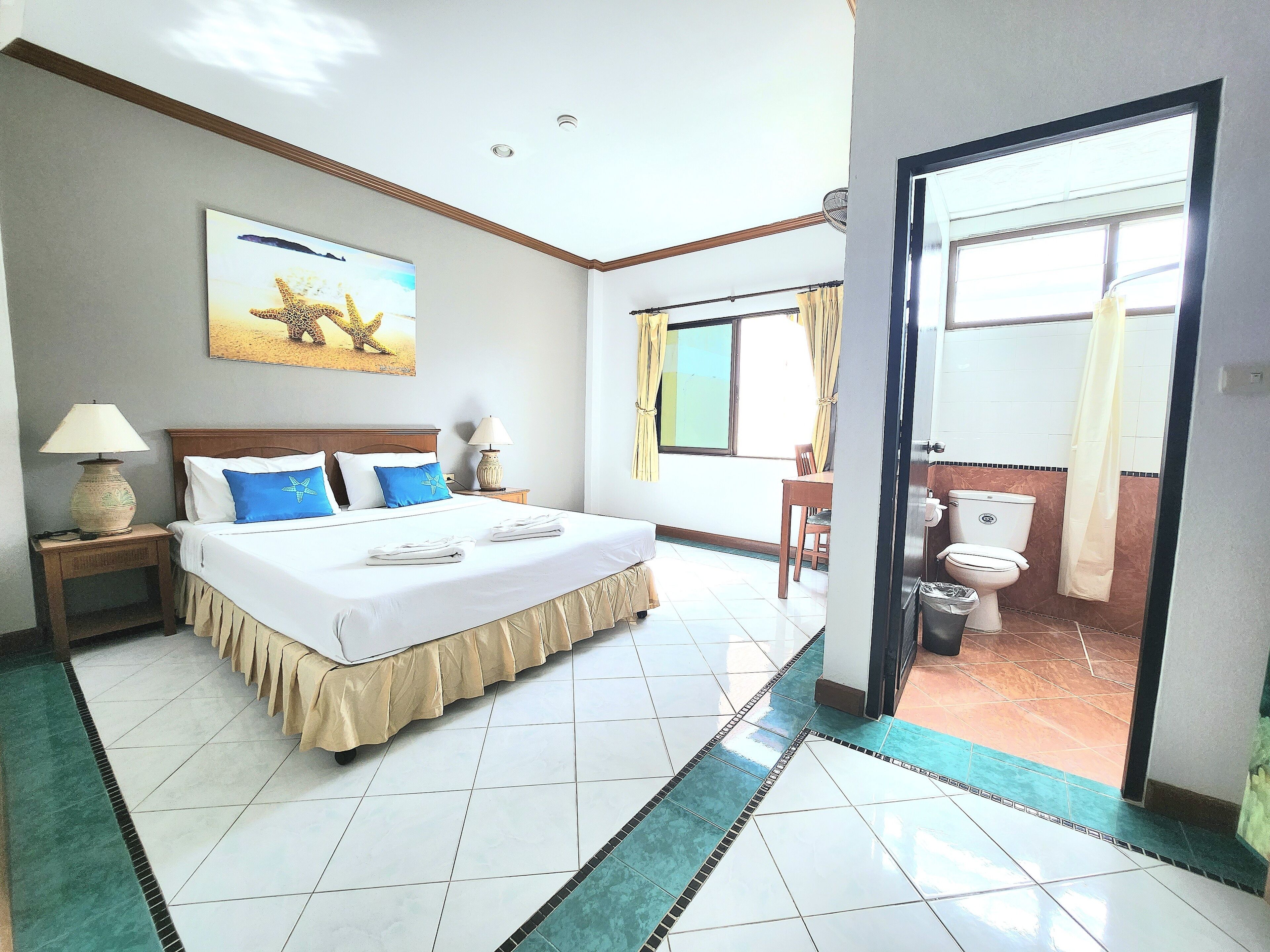Habitación de hotel con cama grande, escritorio, silla, ventana con cortinas, baño con inodoro y lavabo, y puerta que da al exterior.