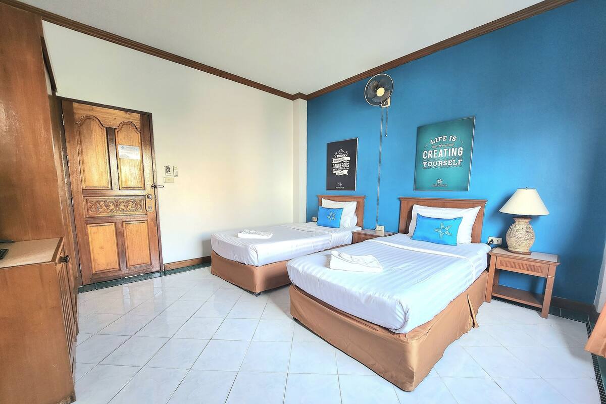 A hotel room with two beds, a wooden wardrobe, a blue wall with motivational posters, and a tiled floor.