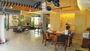 Un vestíbulo amplio con una lámpara moderna, detalles de madera, un mostrador de recepción y un área de descanso.