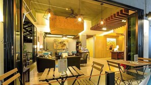Un interior moderno con mesas y sillas de madera, iluminación colgante y una escalera.