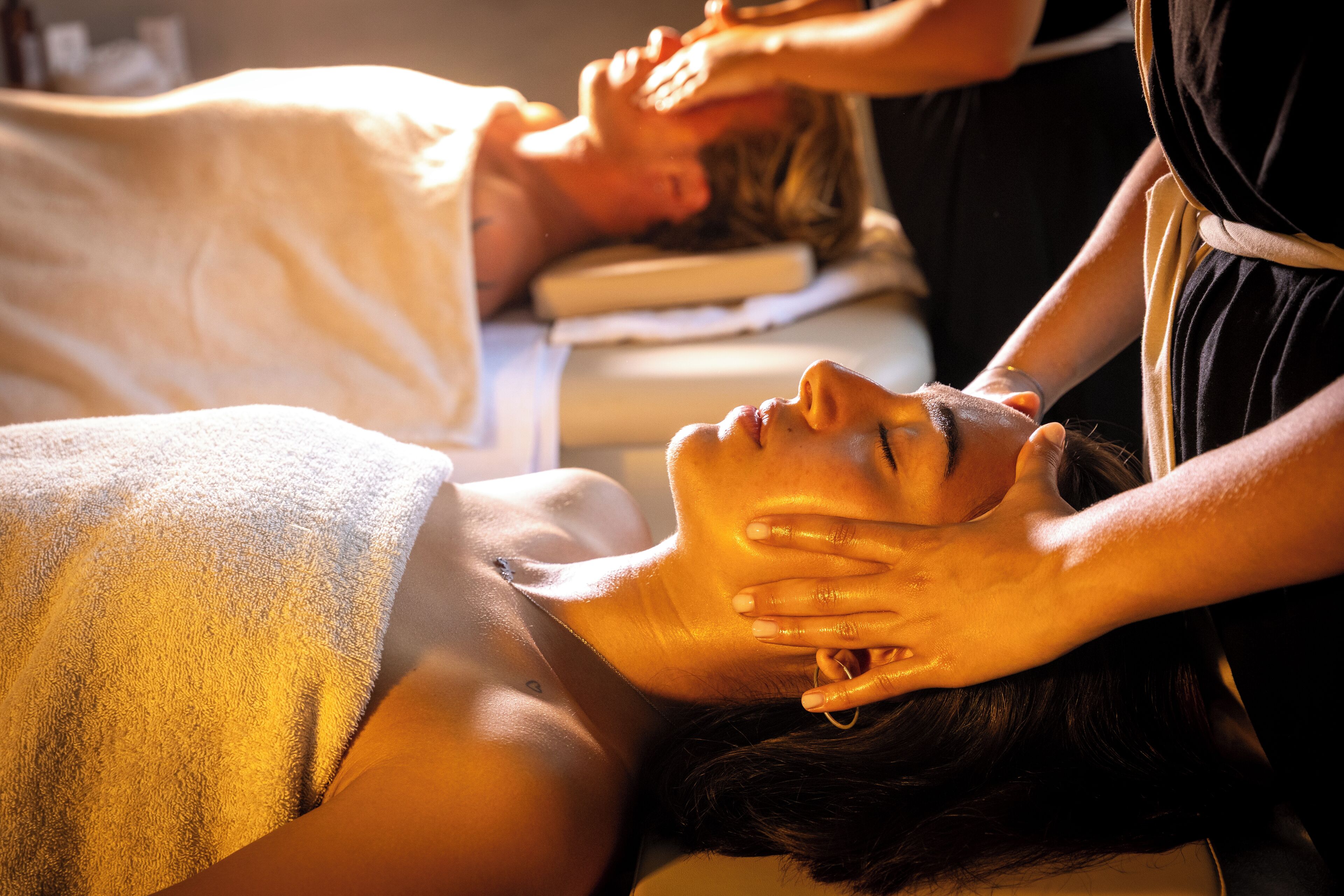 A massage therapy session in a spa setting with a client lying on a treatment table and a therapist attending to them.