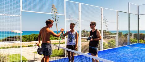 A beach volleyball court with a net, players, and a view of the ocean.