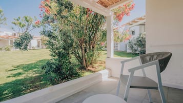 Un portico riparato con una sedia e un tavolo bianchi, affacciato su un giardino con fiori rossi e un prato.