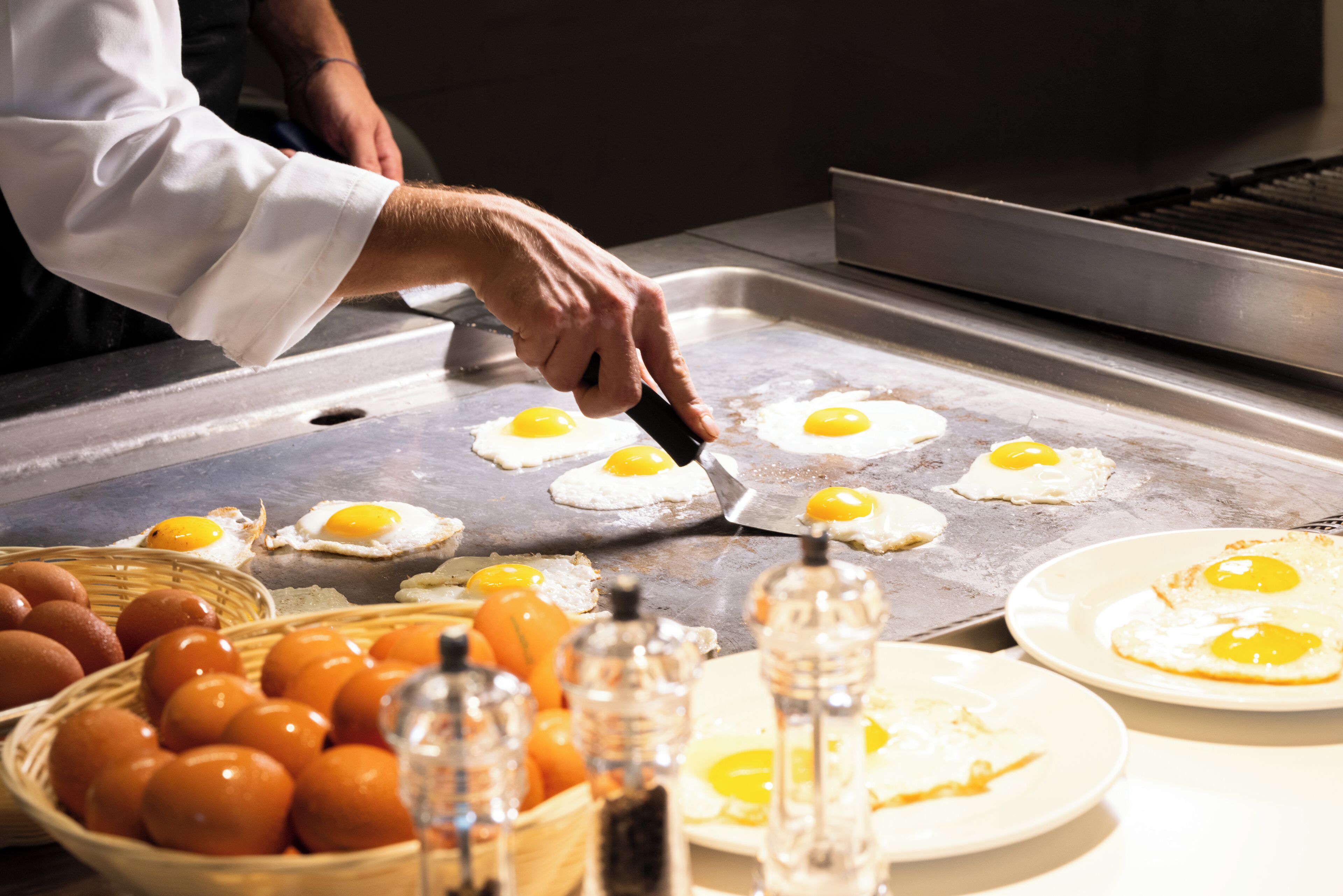 A kitchen with a chef preparing eggs on a griddle.