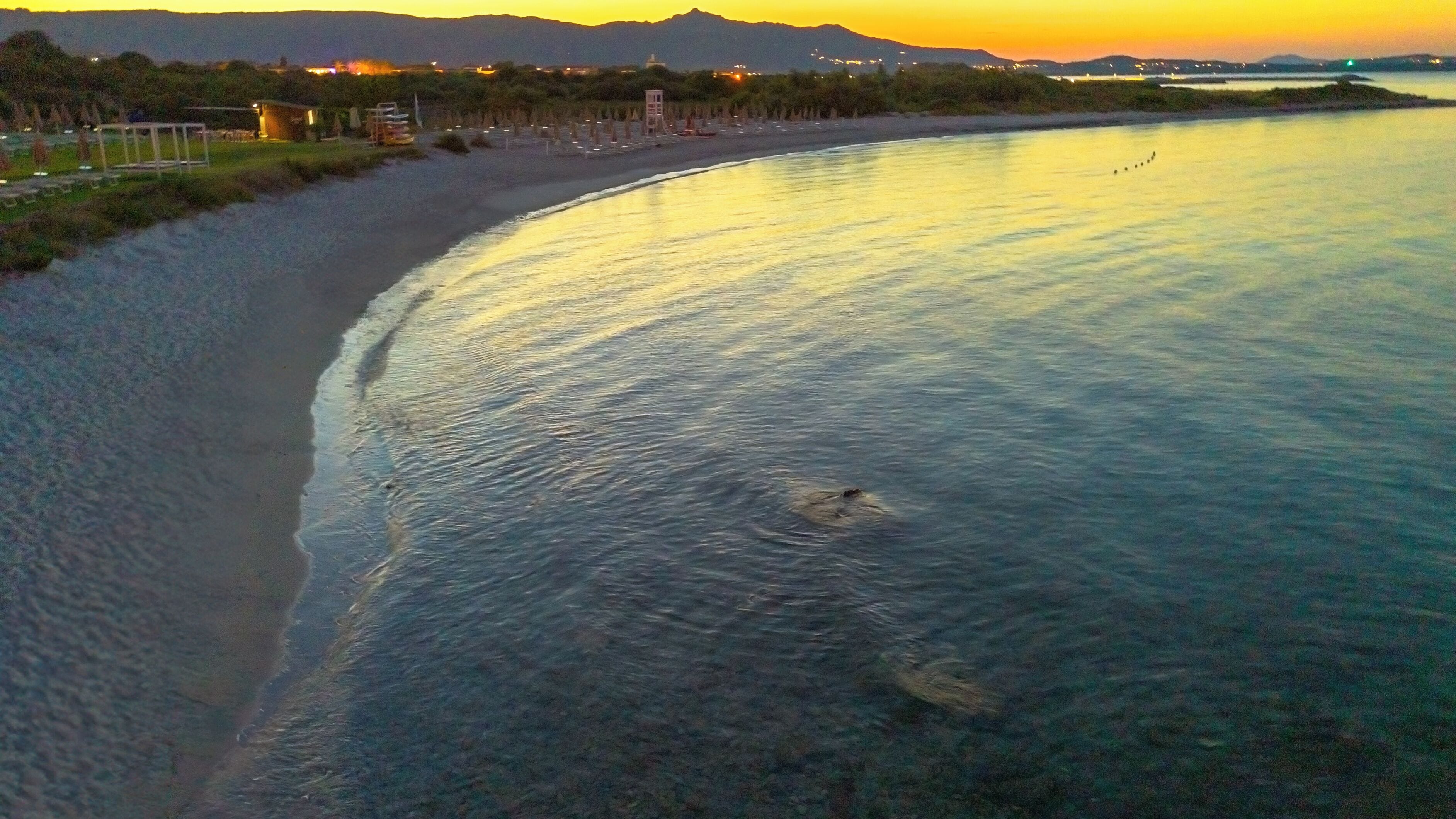 Eine Küstenlandschaft mit Strand, ruhigem Wasser und Bergen im Hintergrund.