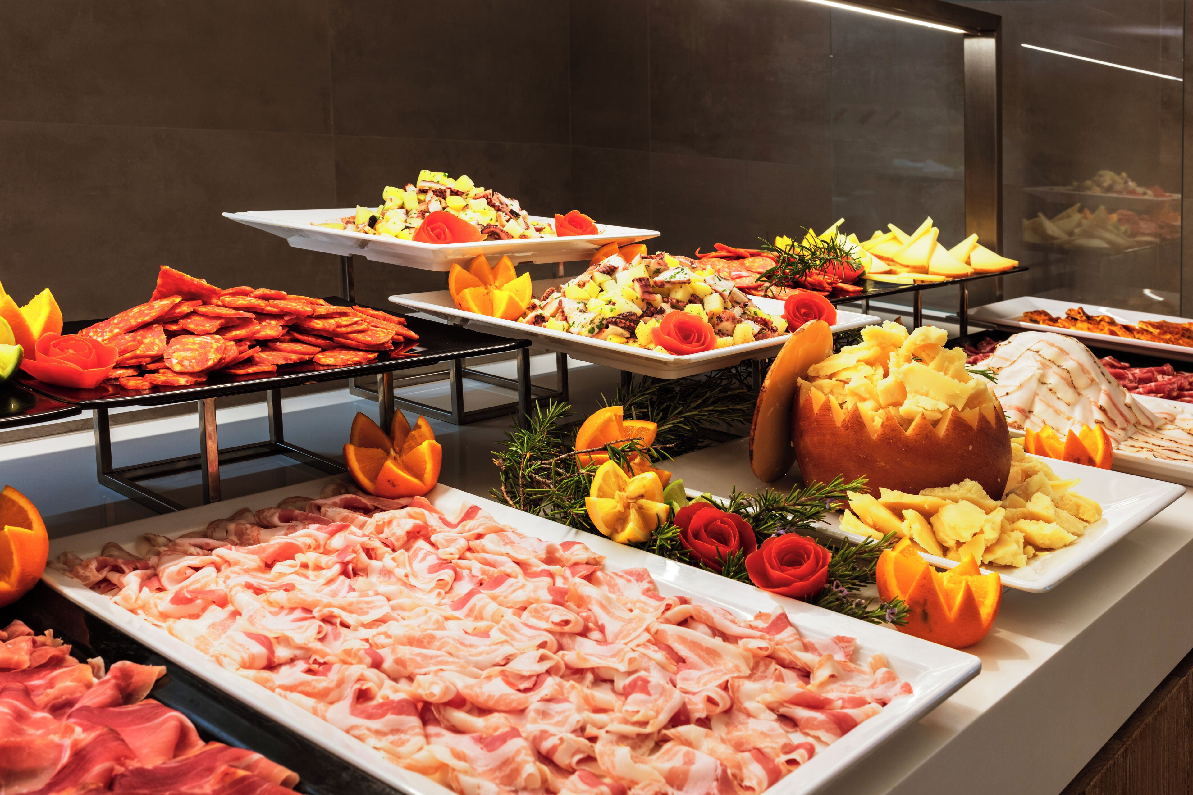 Un bufé con diversas carnes y frutas, incluyendo jamón, tocino y piña.
