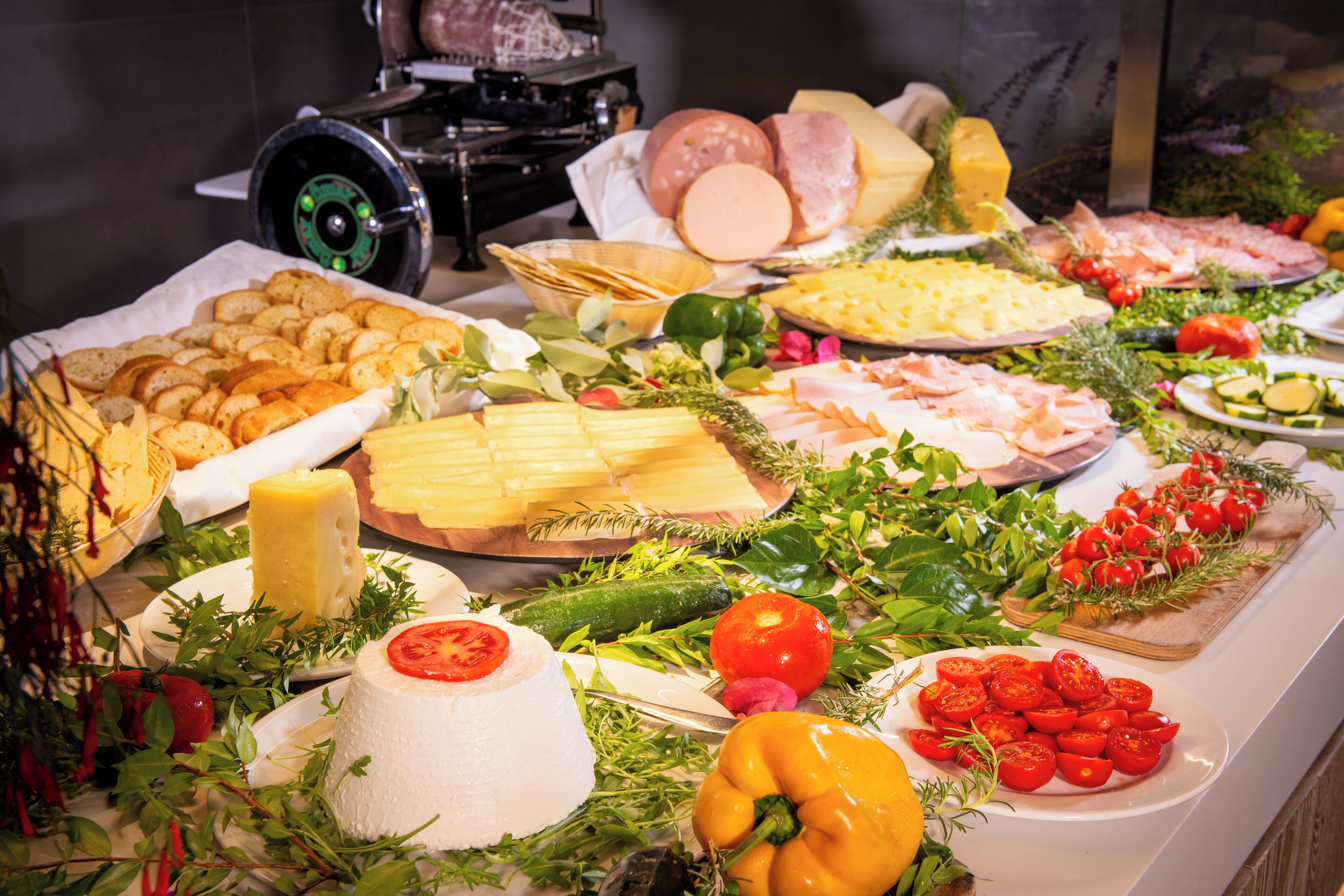 A buffet with various cheeses, meats, and vegetables.