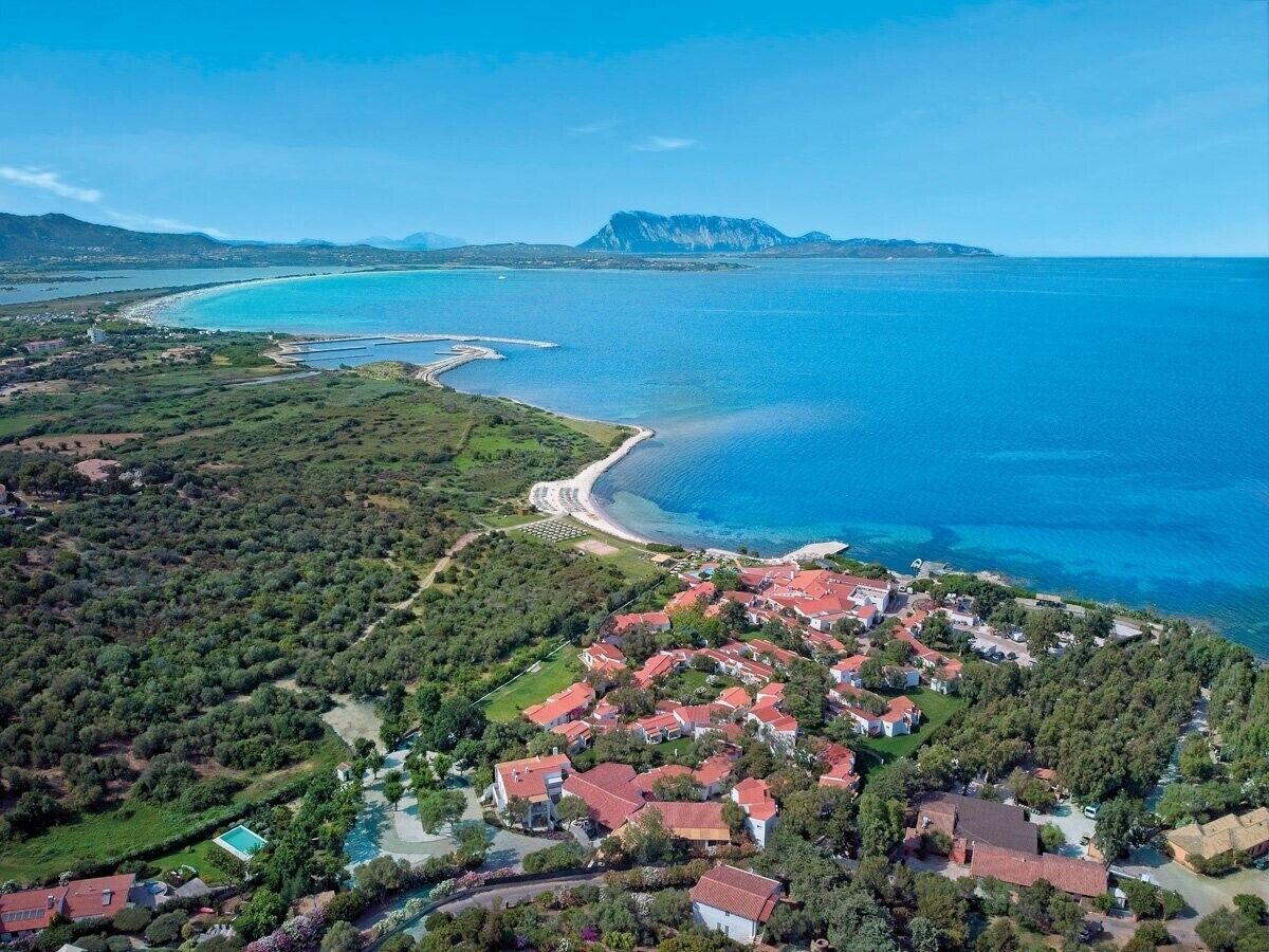 Vista aérea de una zona residencial costera con casas, una playa y una montaña al fondo.