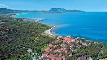 Vista aérea de una zona residencial costera con casas, una playa y una montaña al fondo.
