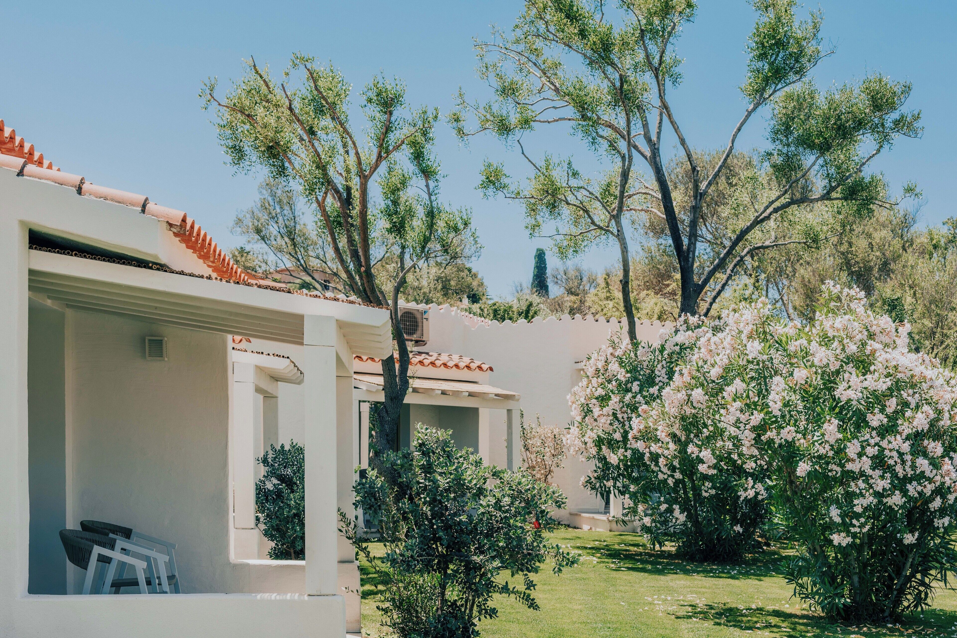 Ein Gebäude mit weißer Fassade, rotem Ziegeldach und einem kleinen Garten mit blühenden Blumen und Bäumen.